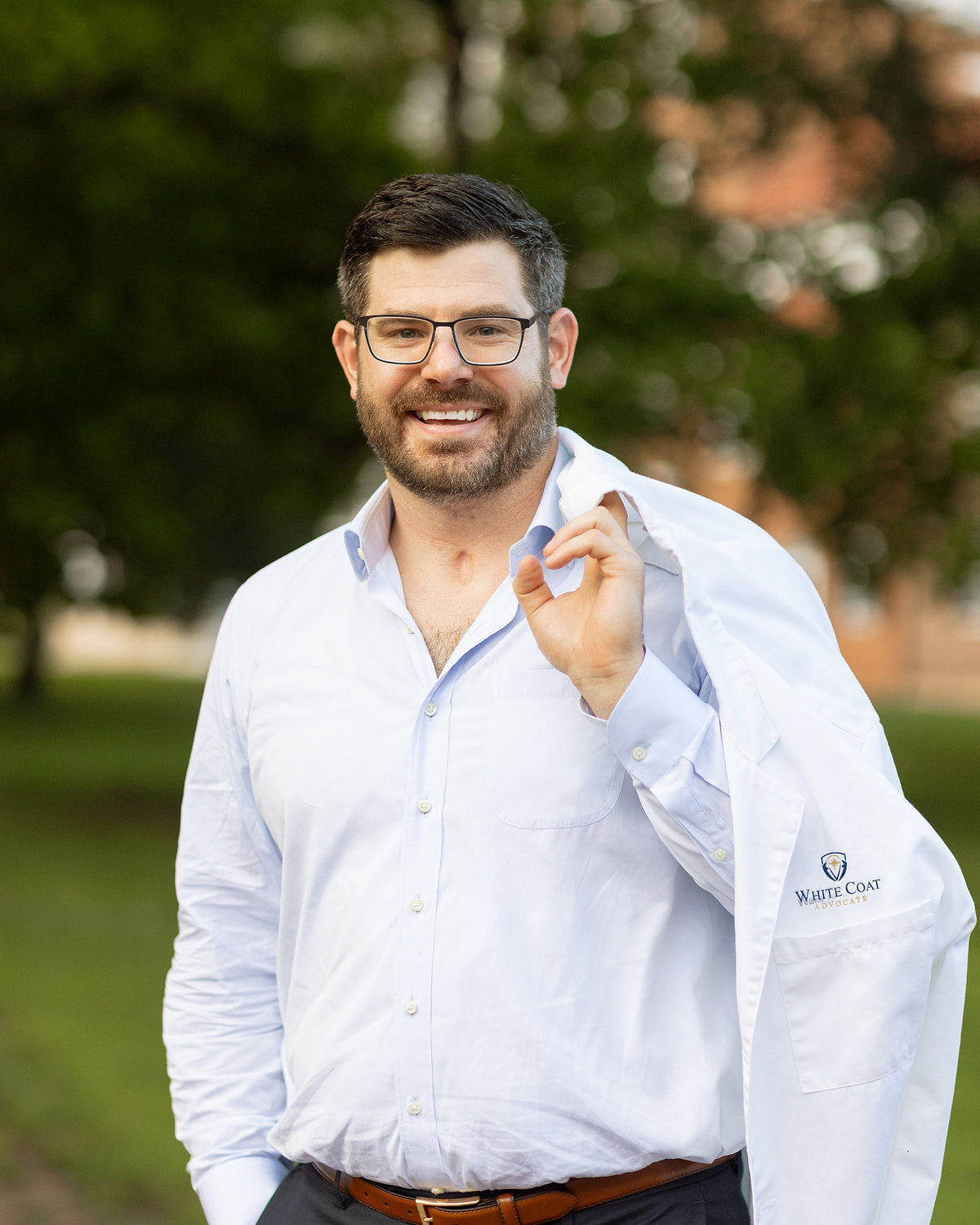 William Dugal, MD, MS, BCPA, holding a White Coat Advocate-branded white coat outdoors