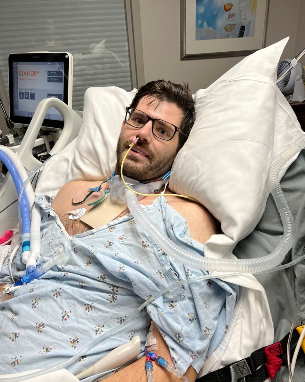 William Dugal in a hospital bed during critical illness, receiving respiratory support
